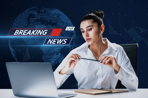 Una presentadora de noticias con camisa blanca frente a su computadora portátil, con un fondo azul que muestra un globo terráqueo digital y el gráfico de "BREAKING NEWS LIVE".