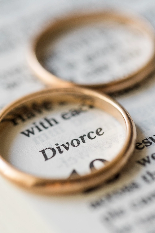 Dos alianzas de boda de oro sobre una página impresa, enmarcando la palabra "Divorce".