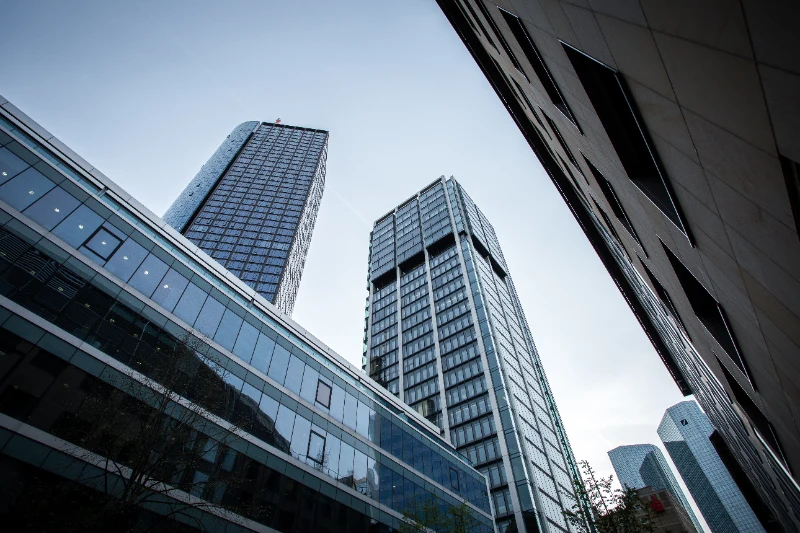 Un contrapicado en perspectiva angular de varios rascacielos corporativos de cristal y acero bajo un cielo despejado.